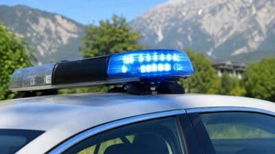 Blaues Blaulicht auf dem Dach eines weißen Polizeifahrzeugs vor Bergkulisse