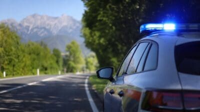 Polizeiauto mit blauem Blaulicht am Straßenrand vor Bergkulisse und Bäumen