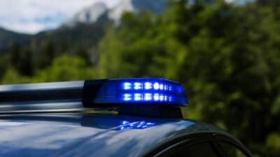 Blaues Blinklicht auf dem Dach eines Polizeifahrzeugs vor bewaldeter Berglandschaft
