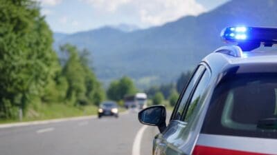 Heckansicht eines Polizeifahrzeugs mit blauem Blaulicht auf einer Landstraße vor Bergen