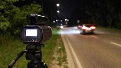 Polizeiliches Radargerät auf Stativ neben einer nächtlichen Straße mit einem Auto im Hintergrund