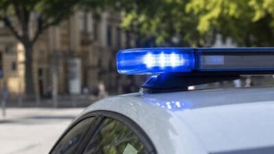 Leuchtendes blaues Blaulicht auf dem Dach eines Polizeifahrzeugs vor unscharfen Gebäuden und Bäumen