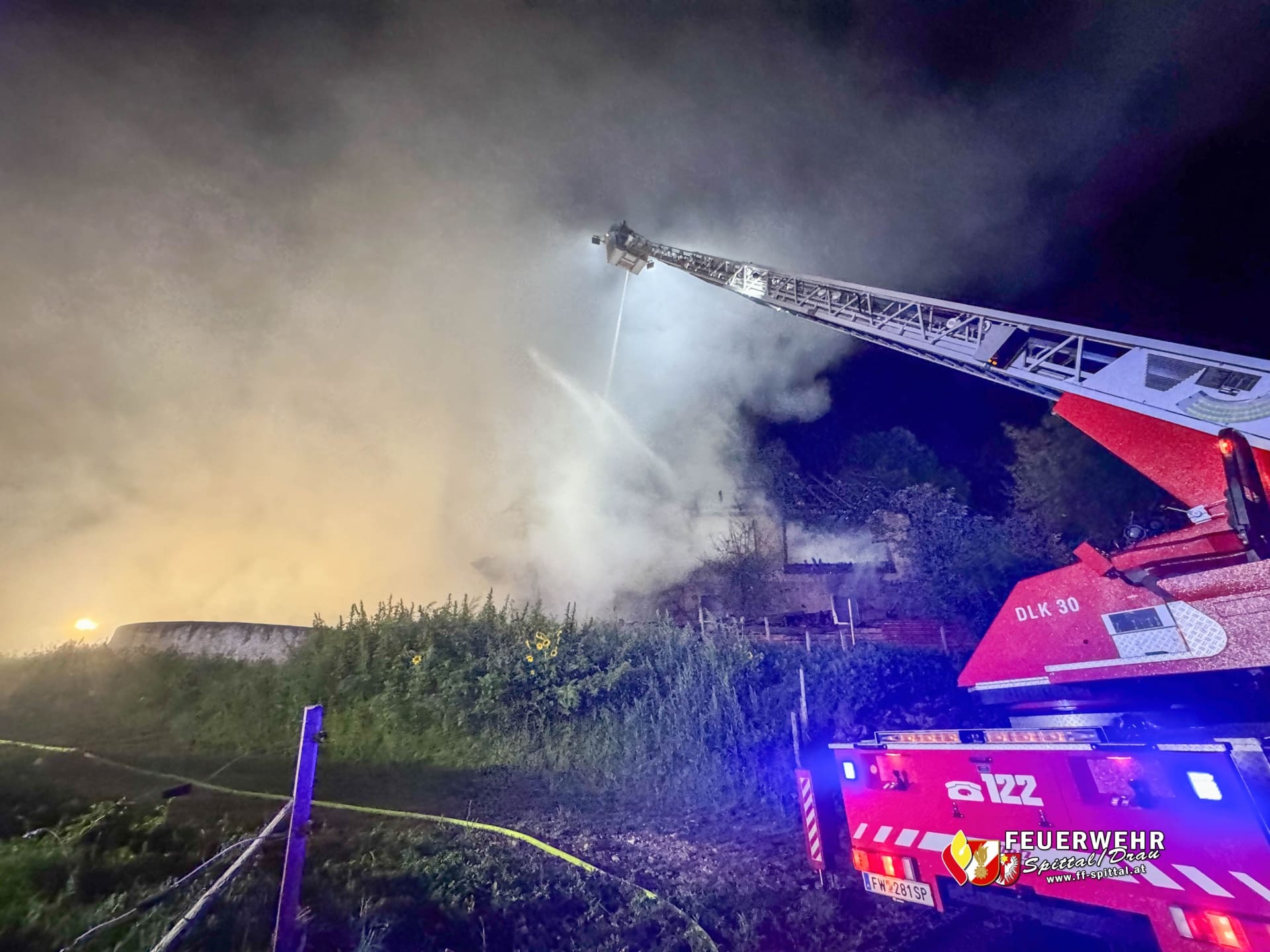 Ausgefahrene Drehleiter eines roten Feuerwehrfahrzeugs löscht brennendes Gebäude in der Nacht