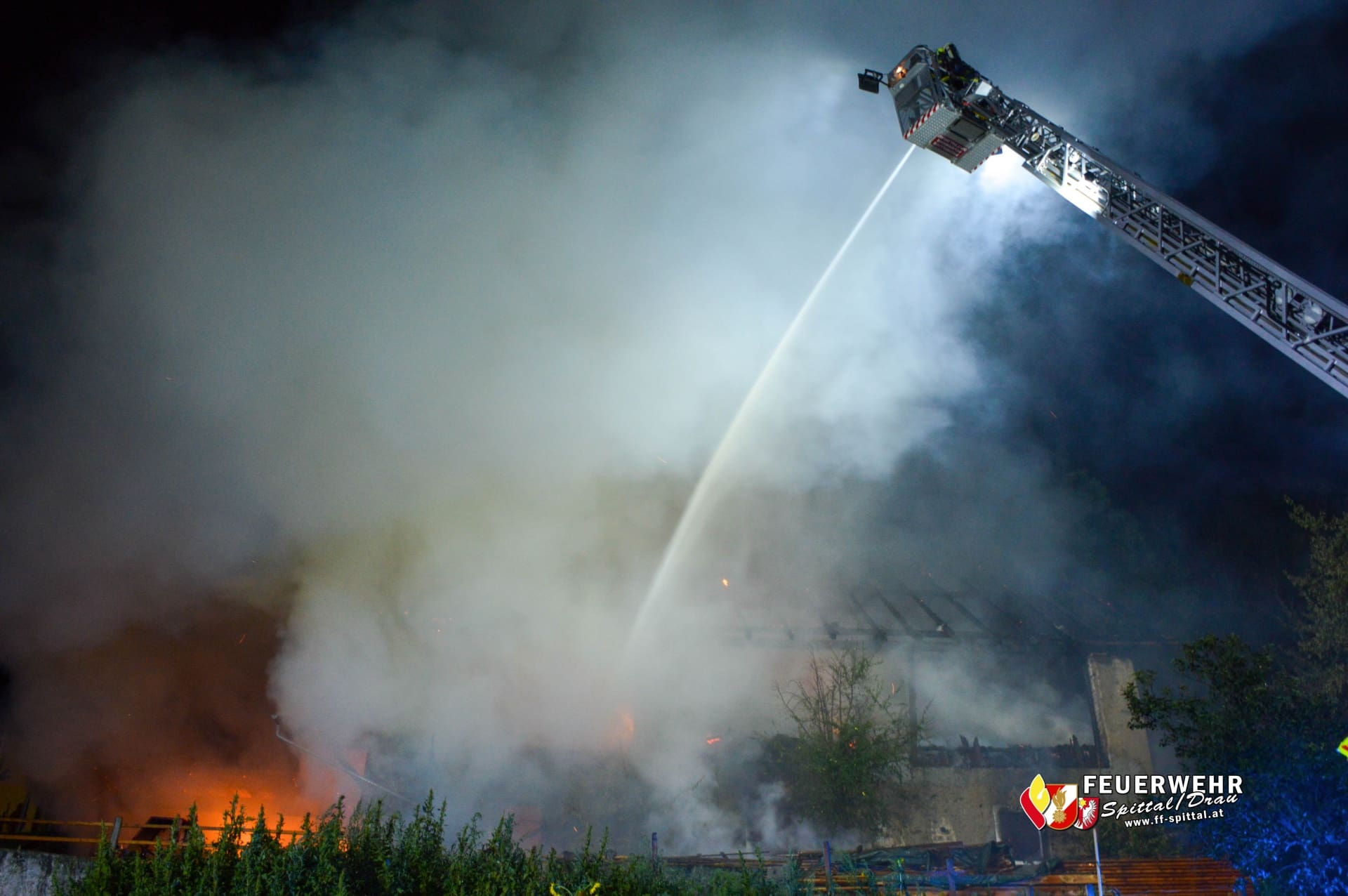 Ausgefahrene Drehleiter der Feuerwehr sprüht bei Nacht einen starken Wasserstrahl in dichten Rauch