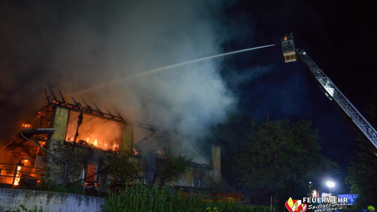 Eine Feuerwehrdrehleiter spritzt bei Nacht Wasser auf ein brennendes Gebäude.