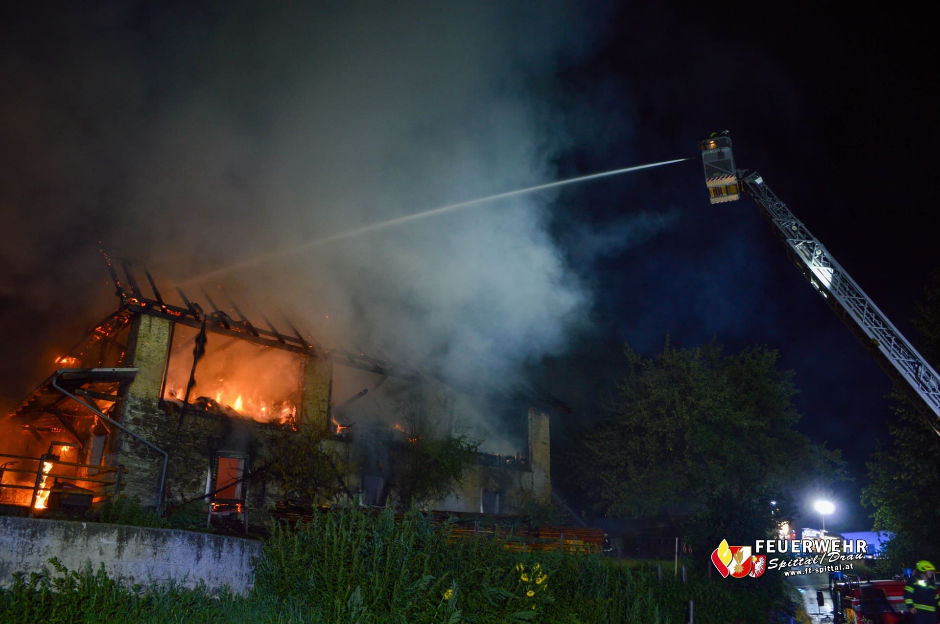 Eine Feuerwehrdrehleiter spritzt bei Nacht Wasser auf ein brennendes Gebäude.