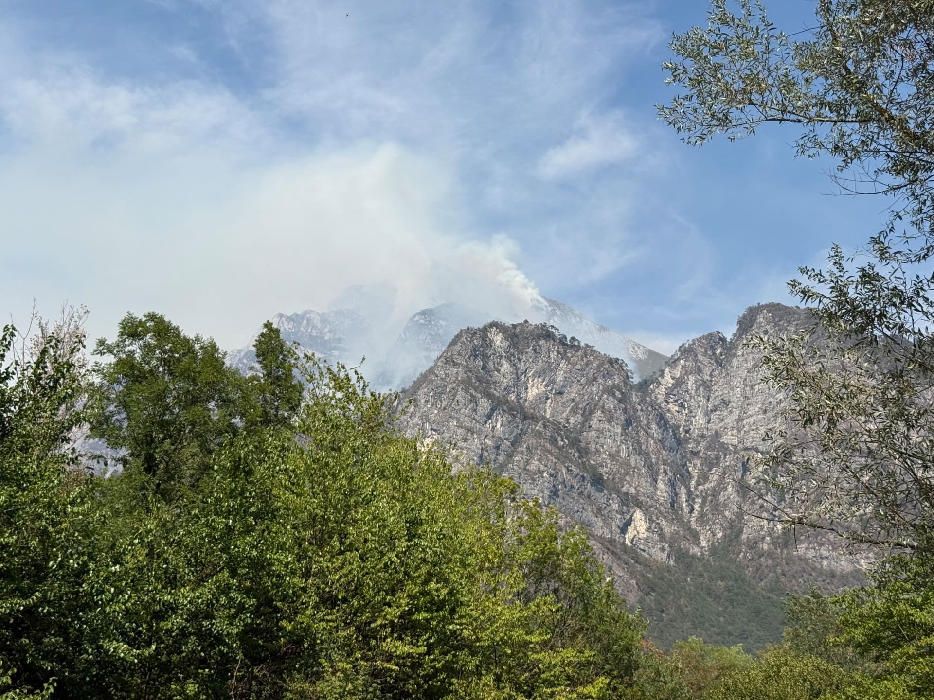 Gebirgszug mit grünen Bäumen und aufsteigender Rauchwolke eines Waldbrands am Monte Amariana