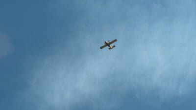 Gelbes Löschflugzeug fliegt durch einen blauen Himmel mit dichten Rauchwolken