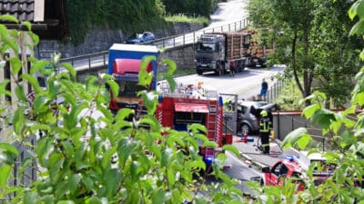 Mehrere rote Feuerwehrfahrzeuge und ein Polizeiwagen am Unfallort mit einem beschädigten Auto.