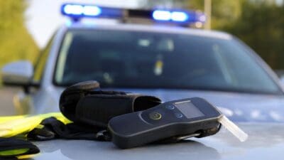 Alkoholtestgerät mit Mundstück auf der Motorhaube eines Polizeiautos mit Blaulicht