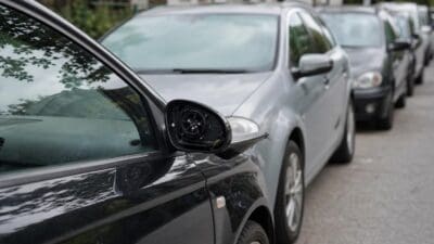 Beschädigter Seitenspiegel an einem schwarzen Auto mit weiteren beschädigten Fahrzeugen dahinter
