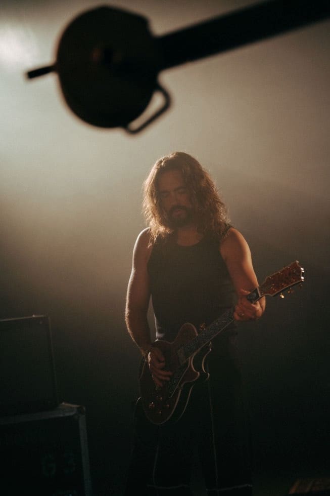 Ein bärtiger Gitarrist mit langen Haaren spielt E-Gitarre auf einer Bühne mit Nebel.