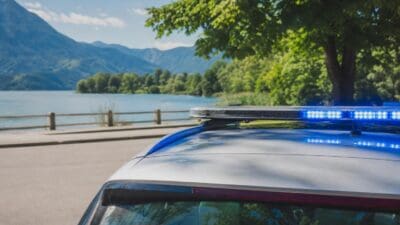 Blaues Blaulicht leuchtet auf dem Dach eines Polizeifahrzeugs vor See und Bergen.