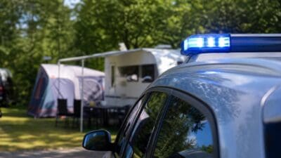 Polizeifahrzeug mit blauem Blaulicht vor einem Zelt und Wohnwagen auf einem Campingplatz