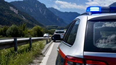 Heck eines silbernen Einsatzfahrzeugs mit rotem Streifen und blauem Blaulicht vor einer Bergkulisse
