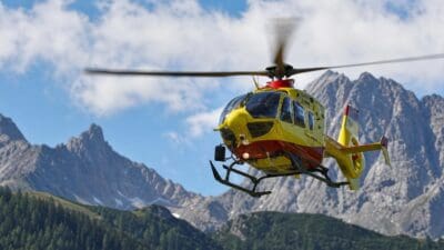 Gelb-roter Rettungshubschrauber fliegt vor schneebedeckten Bergen in Tirol