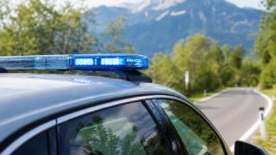 Blaues Blaulicht auf dem Dach eines Polizeifahrzeugs vor Berglandschaft und Straße