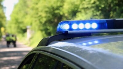 Nahaufnahme des blauen Blaulichts auf dem Dach eines silbernen Polizeifahrzeugs vor grüner Baumkulisse