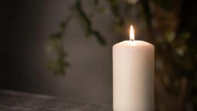 Eine brennende weiße Kerze auf einer dunklen Holzoberfläche vor unscharfem Hintergrund