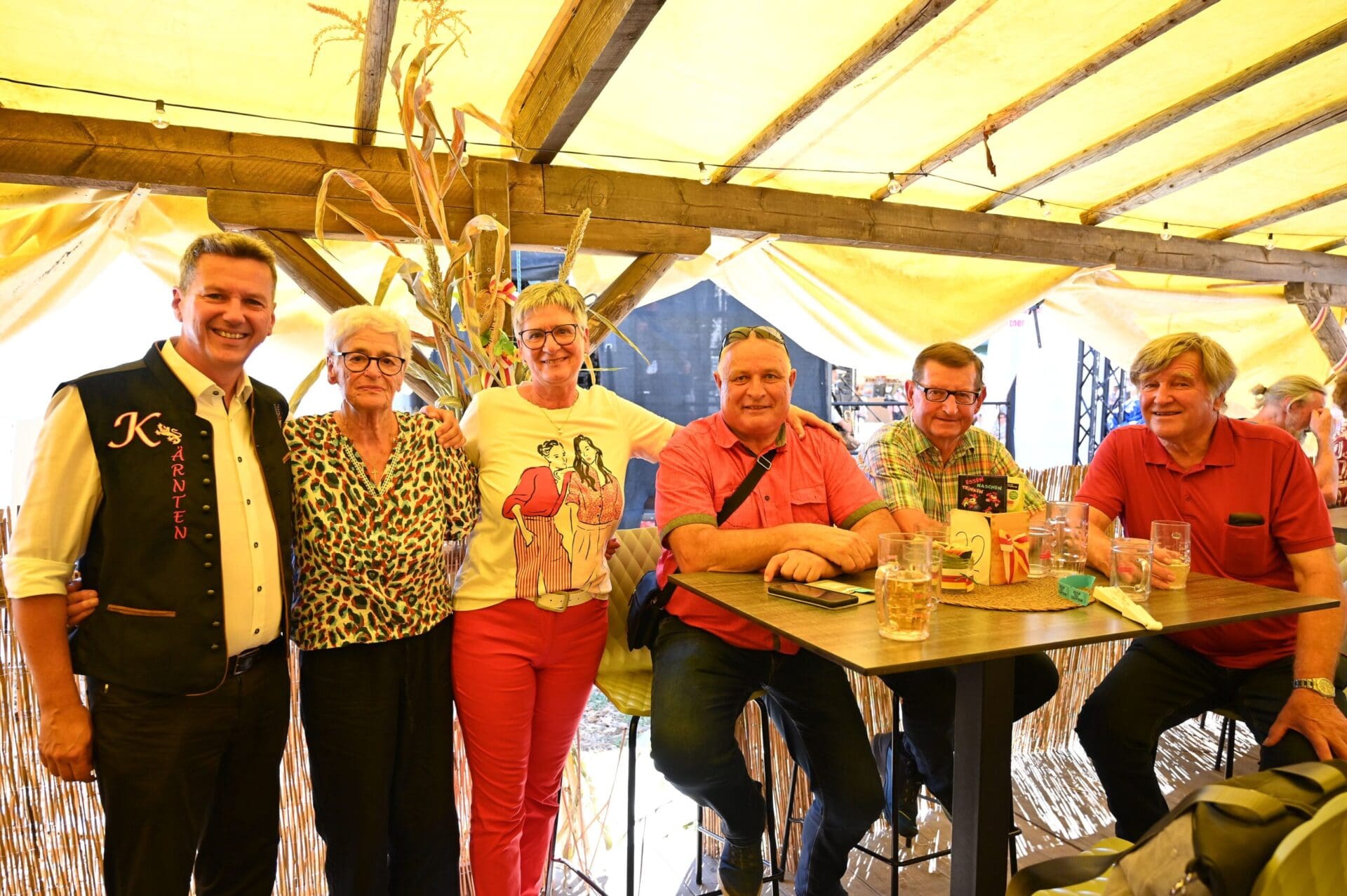 Sechs Personen posieren lächelnd an einem Tisch unter einem gelben Festzelt in St. Andrä.