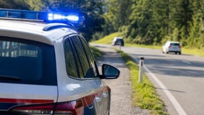 Polizeifahrzeug mit aktiviertem Blaulicht auf einer Landstraße in bewaldeter Umgebung