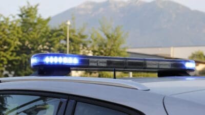 Nahaufnahme eines blauen Blinklichtbalkens auf dem Dach eines weißen Autos mit Bergen im Hintergrund
