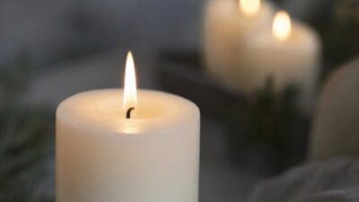 Nahaufnahme einer brennenden weißen Kerze mit heller Flamme und weiteren Kerzen im Hintergrund