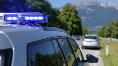 Nahaufnahme des Dachs eines Polizeifahrzeugs mit leuchtendem blauen Blaulicht vor Bergen