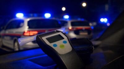 Atemalkoholtester im Vordergrund vor Polizeifahrzeugen mit Blaulicht bei Nacht