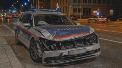 Frontalansicht eines beschädigten Polizeiwagens mit zertrümmerter Motorhaube und Blaulicht in der Nacht