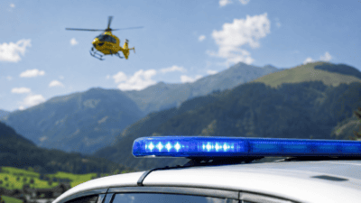 Aktiviertes blaues Blaulicht auf einem weißen Fahrzeug mit gelbem Hubschrauber über Berglandschaft
