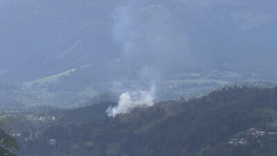 Dichte weiße Rauchwolke über bewaldeten Hügeln in den Bergen am Millstätter See.