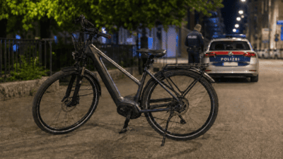 Ein dunkles E-Bike steht nachts auf einer Straße vor einem Polizeiauto mit Blaulicht.