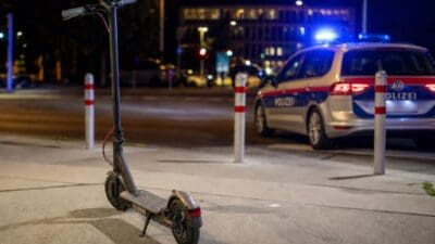 Ein E-Scooter steht nachts auf einem Gehweg vor einem Polizeiauto mit Blaulicht.