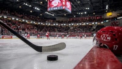 Roter KAC-Helm mit Nummer 17, Eishockeyschläger und Puck auf dem Eis vor Zuschauern in der Arena.