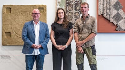 Drei Personen stehen vor antiken Steinreliefs und Mosaiken in einem Ausstellungsraum.