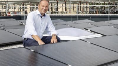Ein Mann in hellblauem Hemd sitzt auf Solarmodulen vor einer Stromverteilungsanlage.