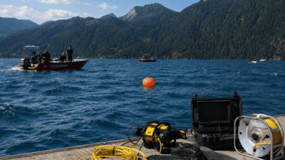 Rotes Feuerwehrboot mit Einsatzkräften auf einem See und Tauchausrüstung mit Roboter im Vordergrund