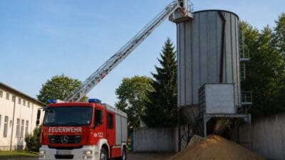 Rotes Feuerwehrfahrzeug mit ausgefahrener Drehleiter an einem Getreidesilo und einem Feuerwehrmann auf der Plattform