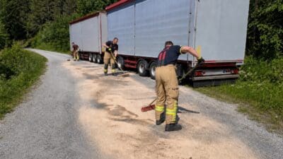 Feuerwehrleute kehren Dieselspuren von der Waldstraße neben einem Sattelzug