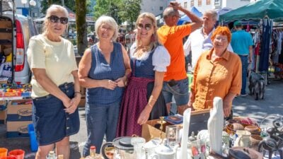 Vier Frauen stehen an einem Tisch mit Glaswaren Vasen und Keramik auf einem sonnigen Flohmarkt