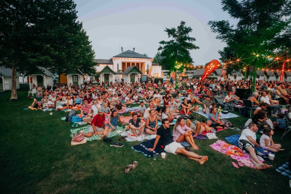 Zahlreiche Menschen sitzen auf Decken auf einer Wiese beim Freiluftkino im Strandbad Klagenfurt