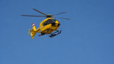 Gelber Rettungshubschrauber mit rot-weißem Heck fliegt vor blauem Himmel