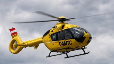 Gelber ÖAMTC-Rettungshubschrauber mit laufenden Rotoren vor grauem Wolkenhimmel