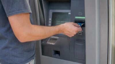 Ein Mann steckt eine blaue Bankkarte in einen grauen Bankautomaten ein.
