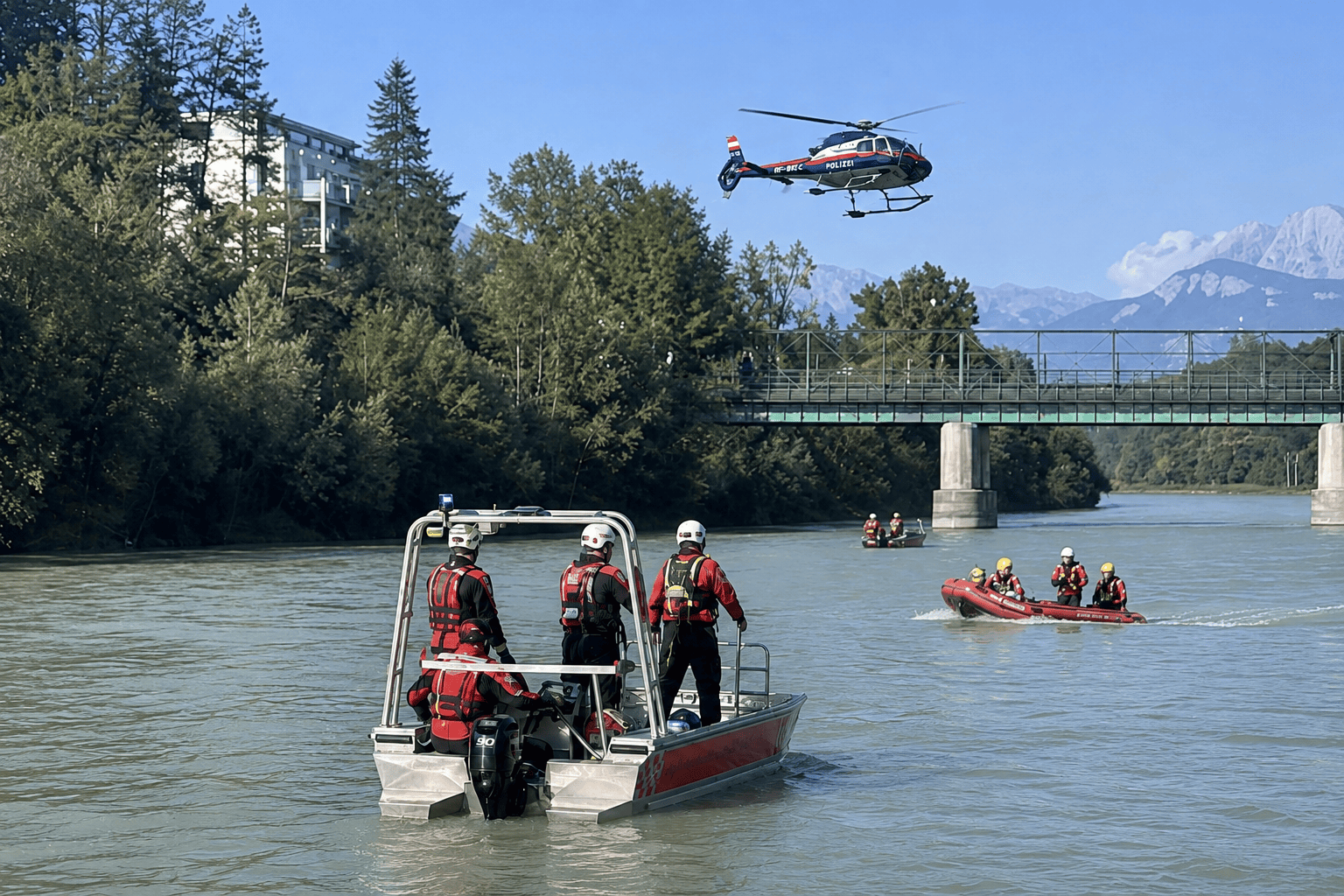Rettungskräfte in roten Booten auf dem Fluss mit Polizeihubschrauber und Brücke im Hintergrund