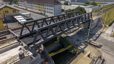 Dunkle Stahl-Fachwerkbrücke wird über einem Wasserlauf auf einer Baustelle montiert.