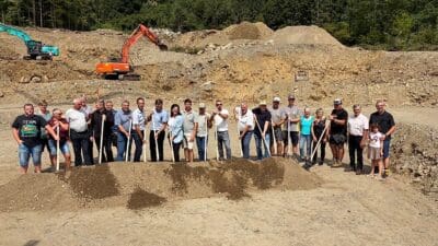 Viele Menschen halten Schaufeln und stehen auf einem Erdhügel vor Baggern auf Baustelle