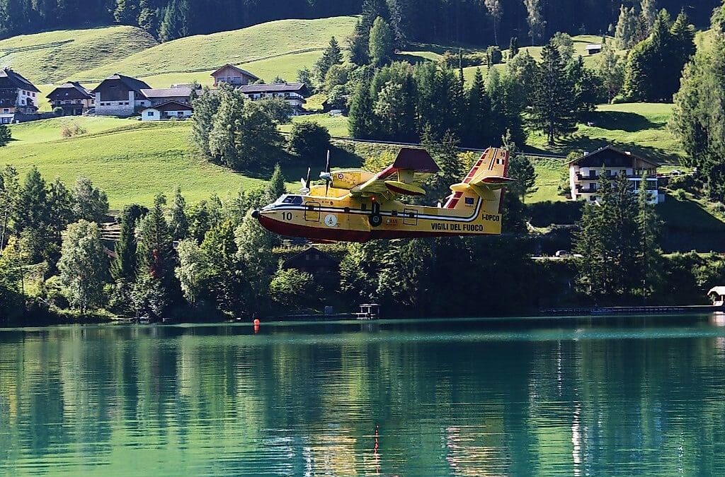 Italienisches Löschflugzeug fliegt über dem Weissensee vor grünen Hügeln und Häusern.