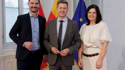 Landesrat Peter Reichmann, Landeshauptmann Daniel Fellner und Landesrätin Marika Lagger-Pöllinger stehen vor Fahnen in einem hellen Raum.